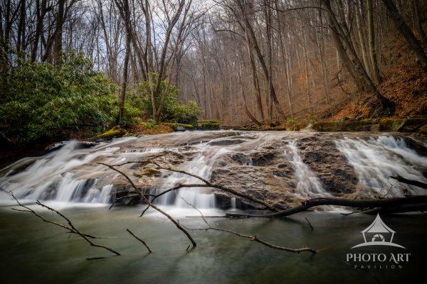 A waterfall flows gently into a blue-green pool, captured in long exposure and surrounded by a quiet