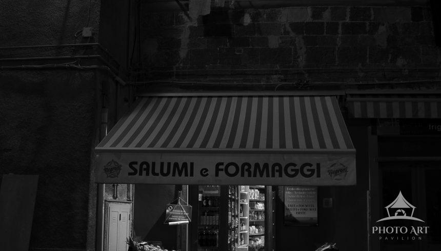 Black and White Deli Reverie presents a quiet urban scene rendered in sharp black and white. A