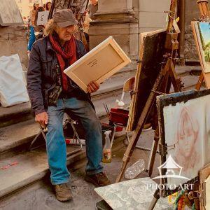 In a candid moment near the Uffizi Galleries, a time-worn street artist sits holding one of his