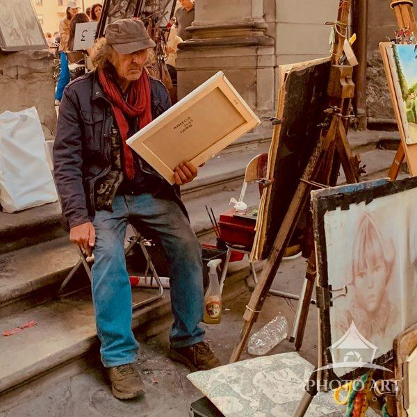 In a candid moment near the Uffizi Galleries, a time-worn street artist sits holding one of his