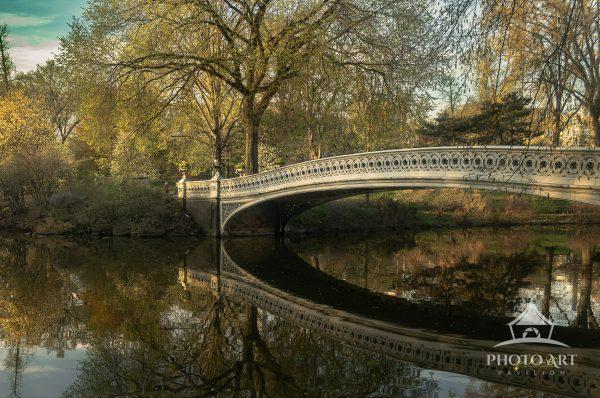 Bathed in warm golden hour light, the iconic Bow Bridge in Central Park stretches gracefully across