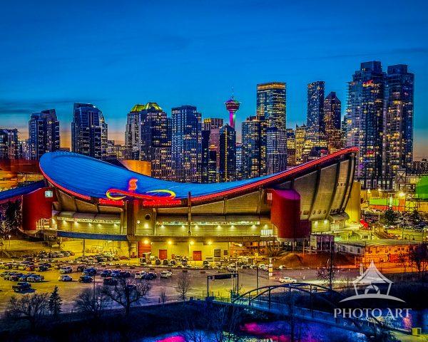 Calgary Saddledome arena lit against the downtown skyline at blue hour, colorful city lights and