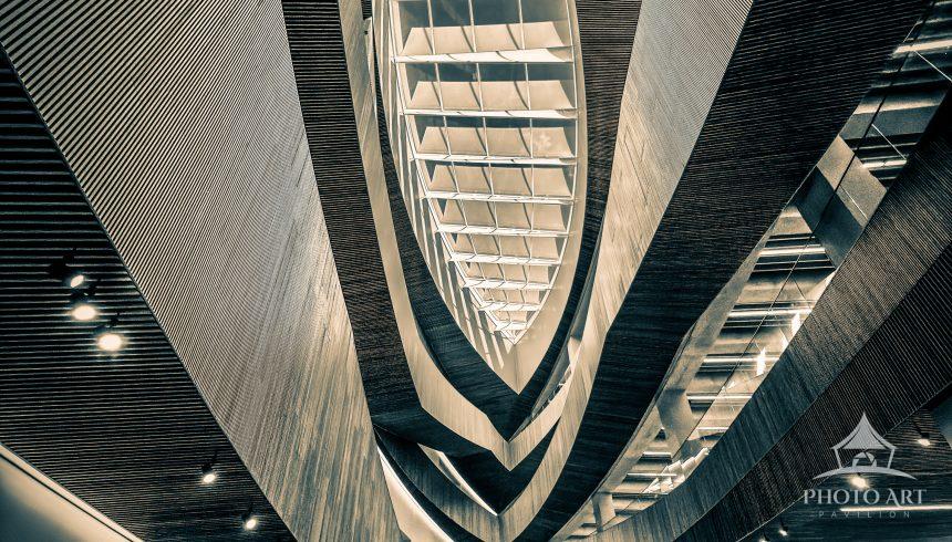 A dramatic modern architecture interior atrium featuring curved wooden balconies, a geometric