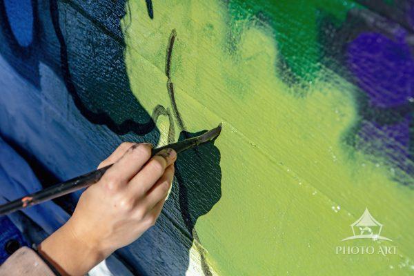 A muralist works on the early stages of a work that will cover the wall of a commercial building.