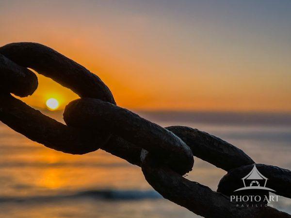 Sun setting over Pacific Ocean captured through a metal chain