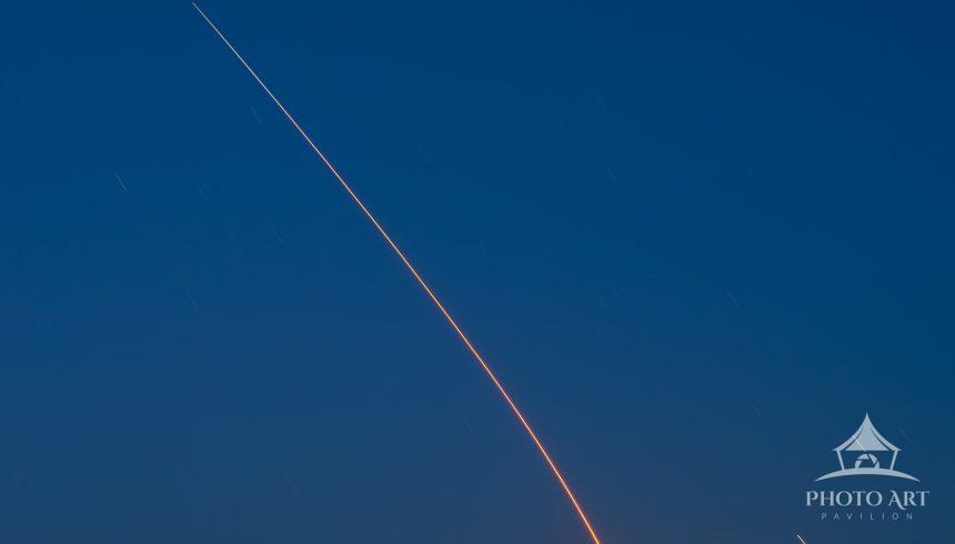 A minimalist image of a rocket launch streak in a cobalt blue twilight sky over Santa Monica Bay,