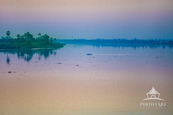 A subtly colorful, tranquil, pre-dawn scene of a lone fisherman on the Nile River in Egypt. 1st
