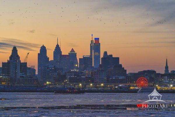 A landscape photograph showcasing the Philadelphia skyline silhouette captured at dusk from across