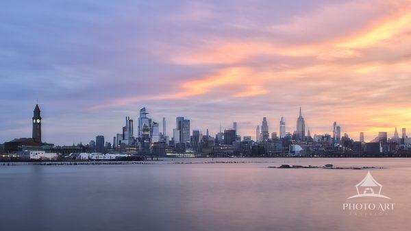 A tranquil pre-sunrise view captured from Newport, New Jersey, featuring soft pastel clouds painted