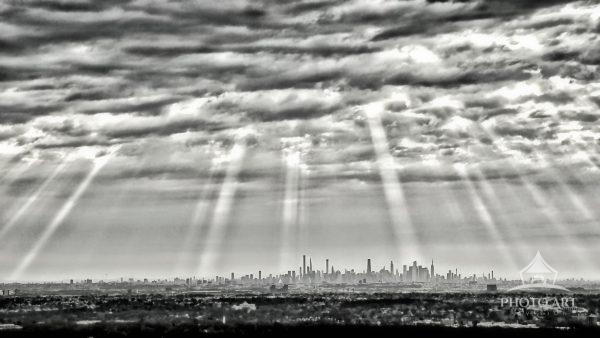 A dramatic, high-contrast black and white photograph capturing a panoramic view of the distant New