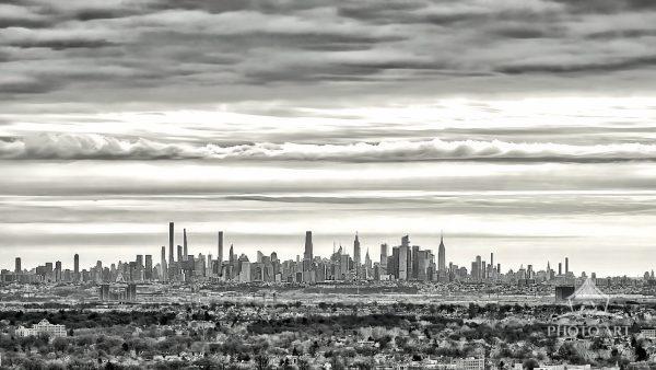 A high-contrast, black-and-white photograph capturing a panoramic view of a massive urban skyline