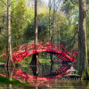 The artwork features a vibrant red arched wooden bridge spanning across a small body of water. The
