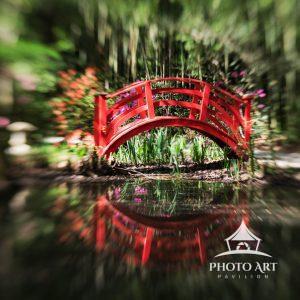 The artwork depicts a vibrant red arched bridge spanning across a calm body of water. The bridge