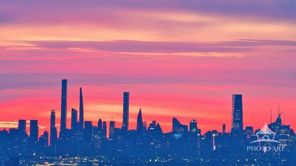 This image displays a telephoto view of the New York City skyline silhouetted against a dramatic