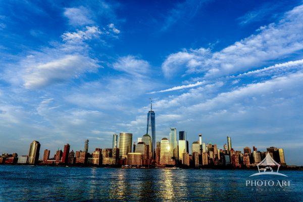 Manhattan rises beneath an expansive blue sky, where light, water, and architecture come together in