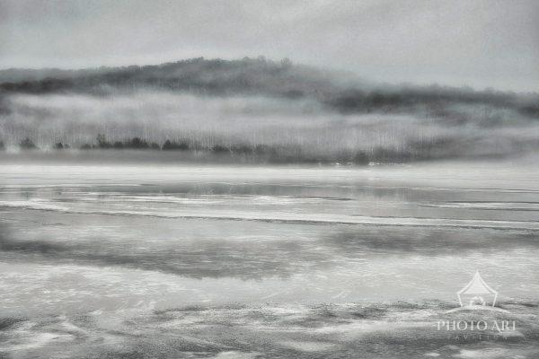 This expansive monochrome photograph captures thick morning fog rolling low over the frozen expanse
